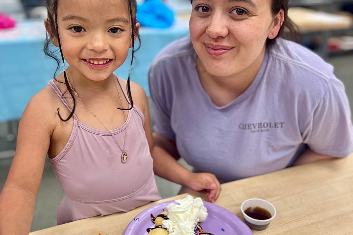 Smiling child and adult sitting at a table with dessert on a plate. Sprinkles and syrup on pancakes visible.