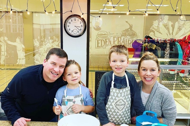 Family of four smiling while baking, with kids wearing aprons, in a bright kitchen.