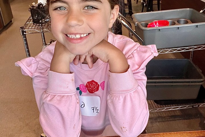 Girl smiling at a table in a café with a pink sweater.