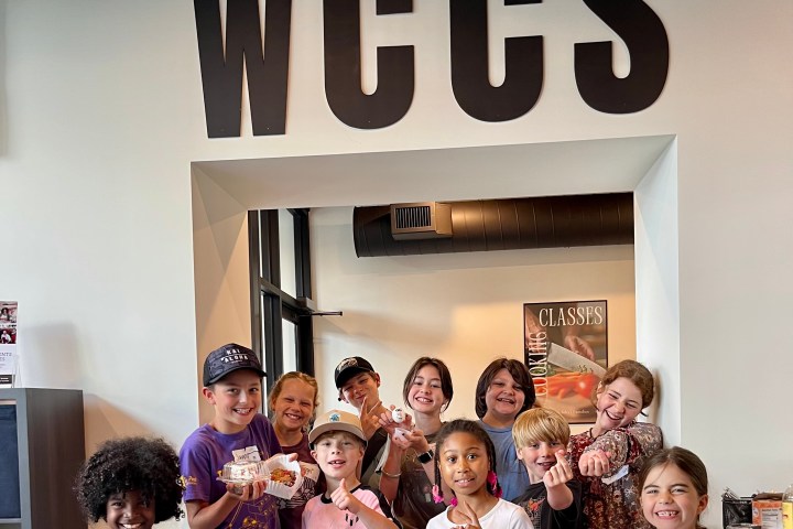 Group of smiling kids and adults in a room with 'WCCS' sign above.