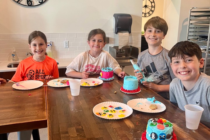Four kids smiling at a table with decorated cupcakes and drinks.
