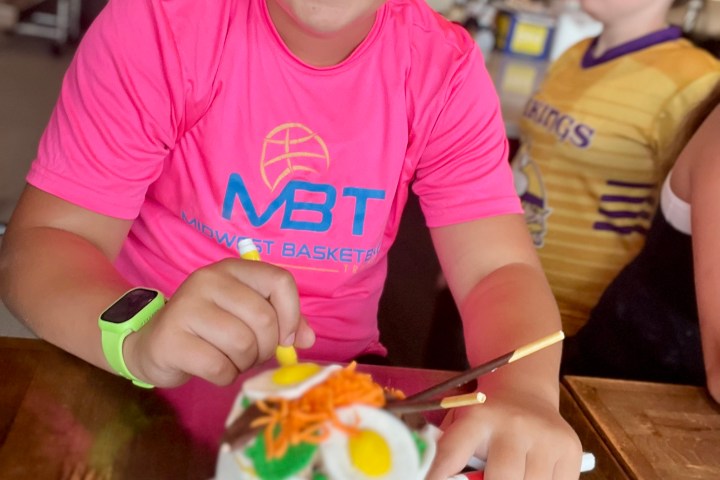 Smiling child with cake on a wooden table in a kitchen setting.