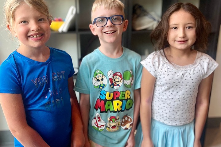 Three smiling children stand in front of shelves with display materials.