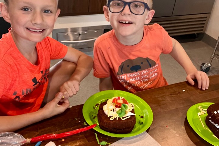 Two boys smiling with decorated cakes on plates indoors.