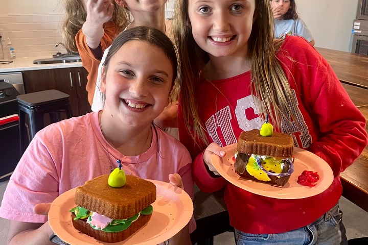 Four kids smiling, holding plates with creative food art resembling burgers made from cookies and candy.