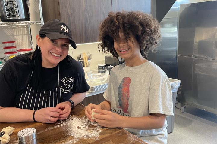 Two people smiling while preparing dough in a kitchen.
