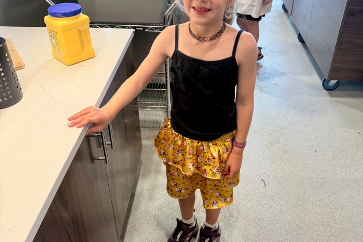 Smiling child in kitchen with a black top and golden skirt.