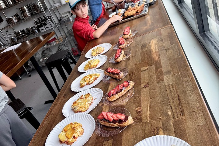 Children preparing pastry dishes on a wooden counter in a kitchen.