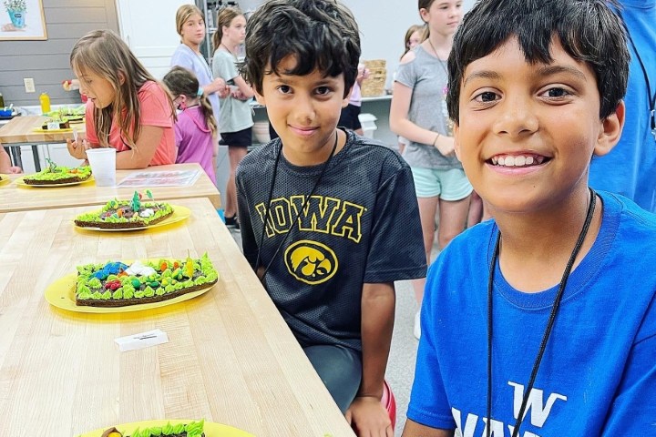 Two boys smiling at a table with decorated cakes on plates during a group activity.