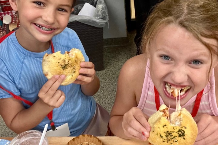 Two smiling kids eating cheesy pastries at a table with empty dishes and a smoothie.