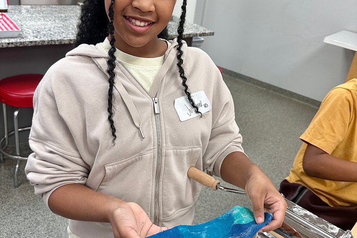 Smiling girl holding rolled-out blue dough in a kitchen.