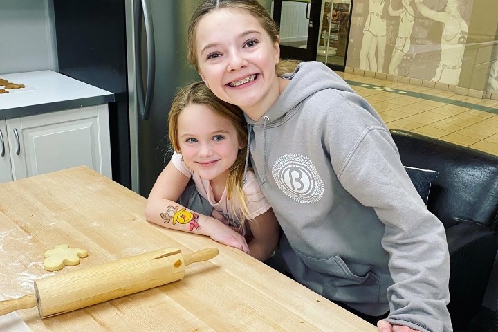 Two smiling children pose in a kitchen near a rolling pin and cookie dough.