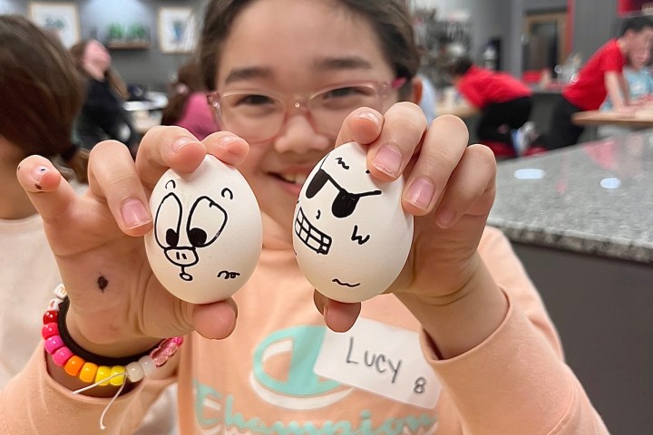 Child holds two eggs with cartoon faces in a kitchen setting.
