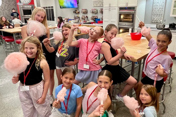 Group of kids smiling and holding cotton candy in a colorful room with tables and decorations.
