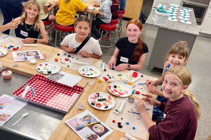 Kids seated at a table in a craft class, making colorful clay art on plates.