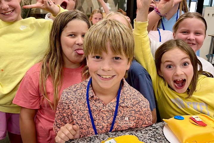 Group of smiling children with decorated cakes on a granite countertop.